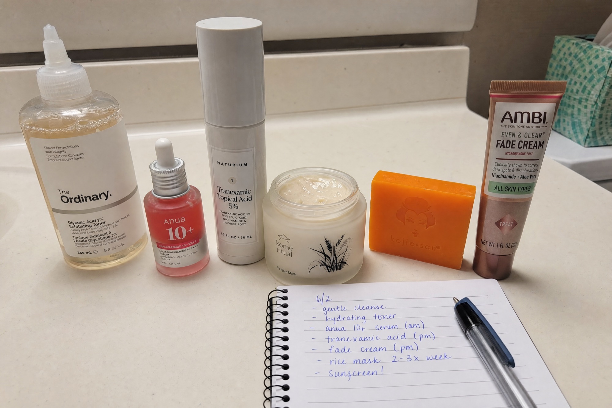 The six dark-spot products we tested, laid out on a bathroom counter with a reviewer's notebook